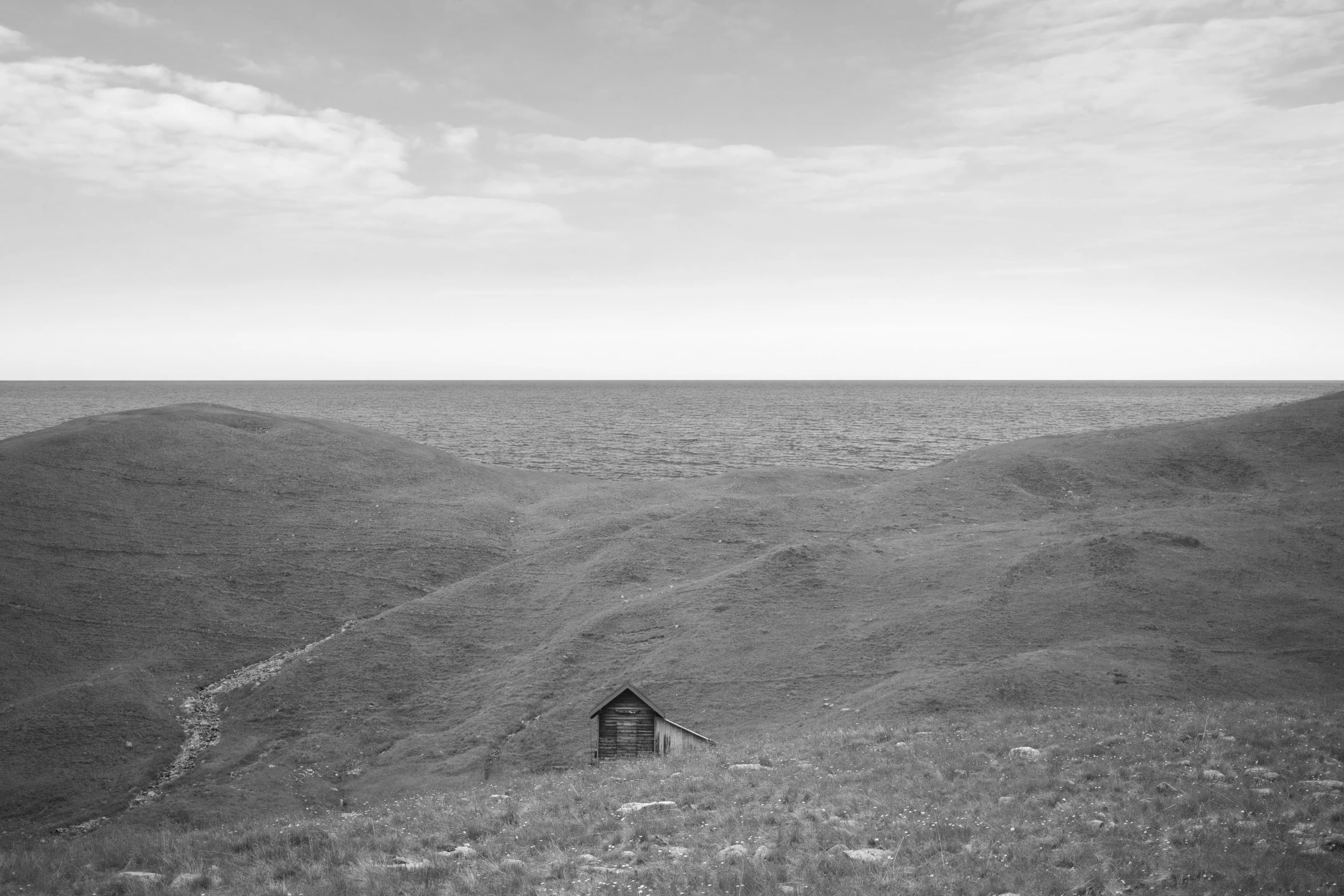 The same hut on rolling hills above a calm sea under a cloudy sky