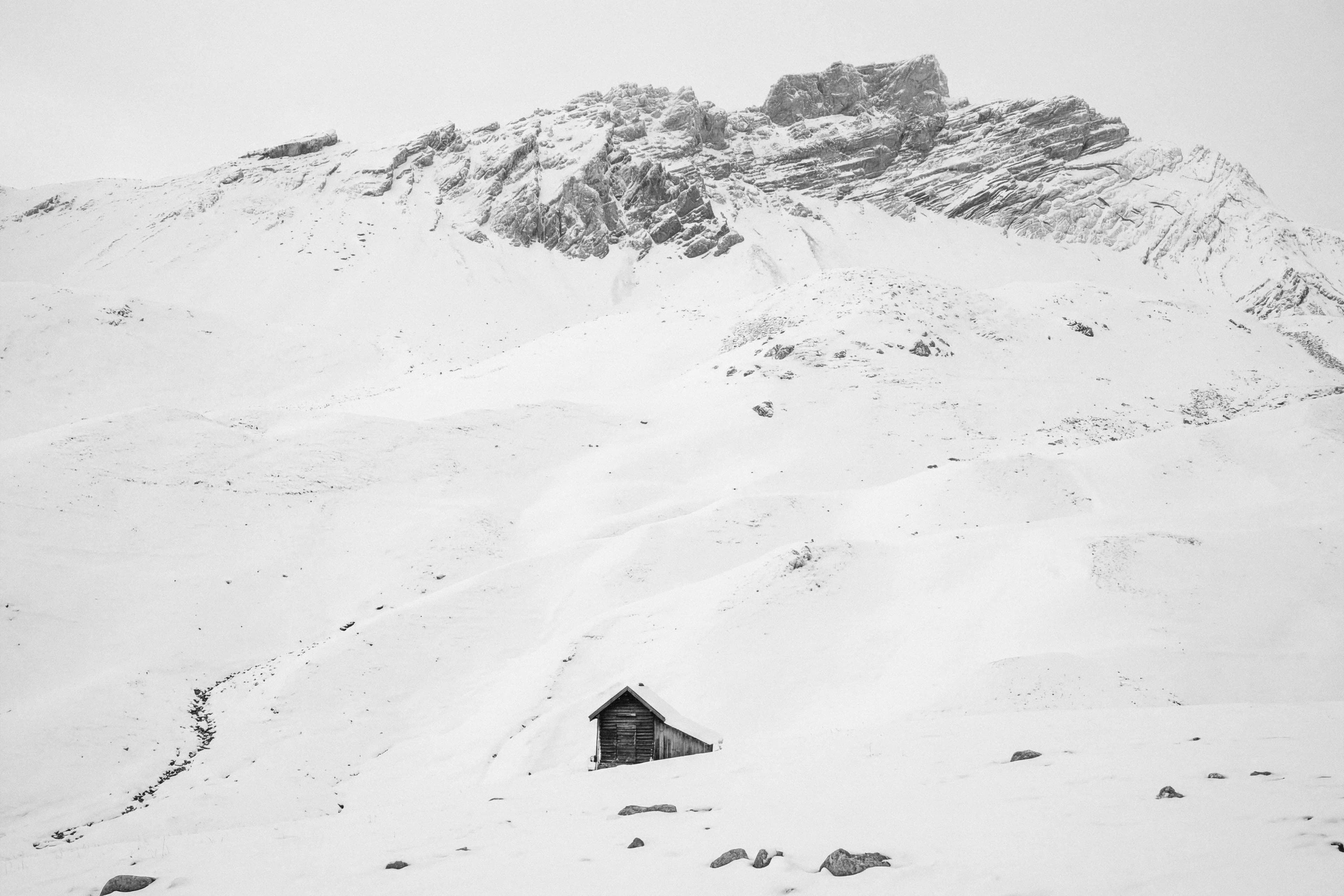 The mountain scene under deep snow with the hut on a snowy slope